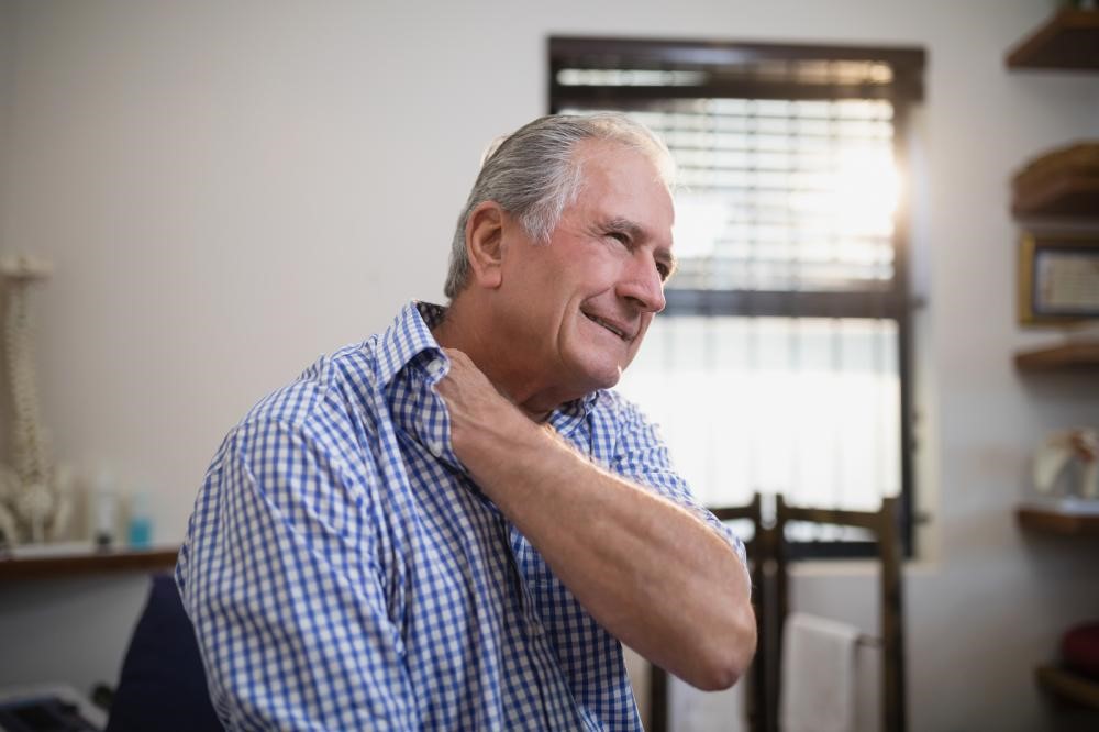 An older man grimacing in neck pain and touching his neck.