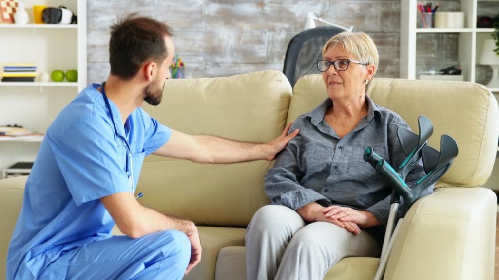 A male physical therapist reassuringly talks to an older woman with Parkinson’s