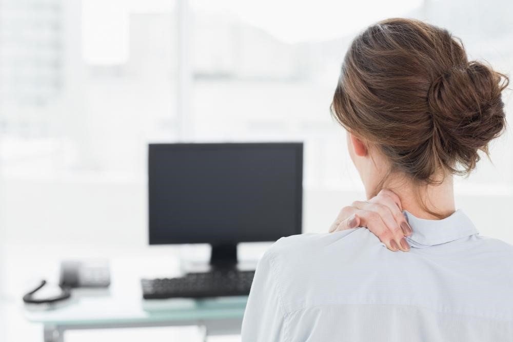 A working woman presses her fingers against her neck to alleviate neck pain.
