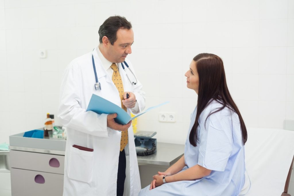 A doctor talks to a woman in a clinic patient exam room.