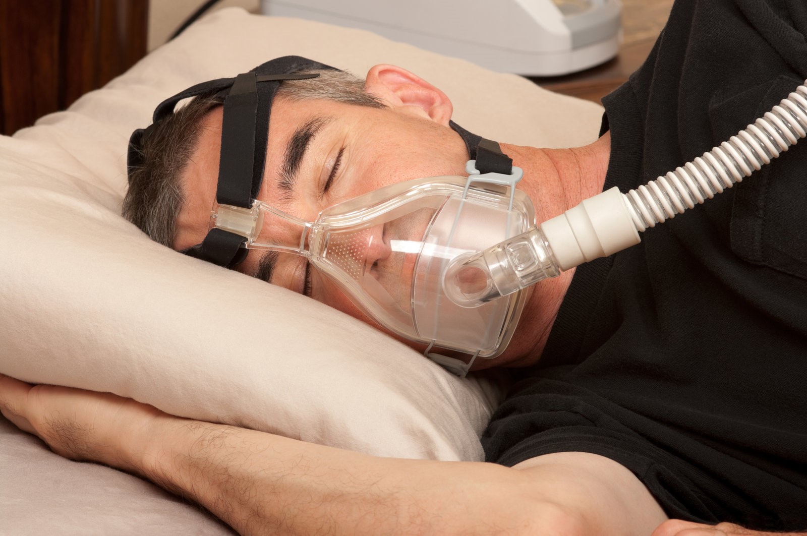 A man sleeping in his bed with a CPAP machine attached.