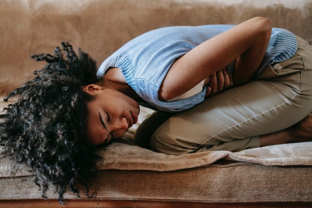 A woman bent over in pain from PMS on a couch.