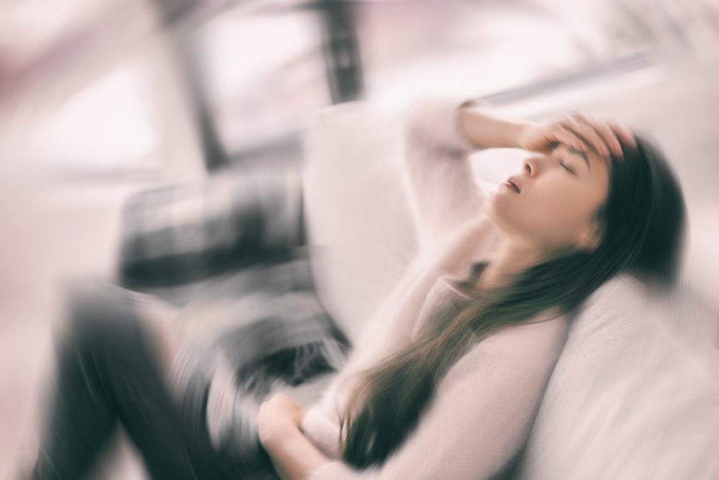 A woman collapsing on a sofa from vertigo dizziness.