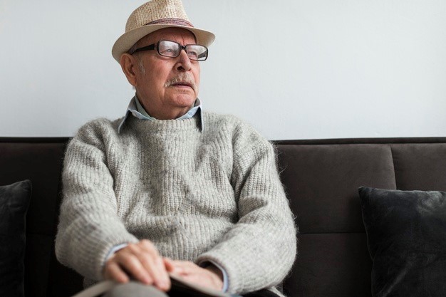 an elderly man sitting on a black sofa waiting for a seizure