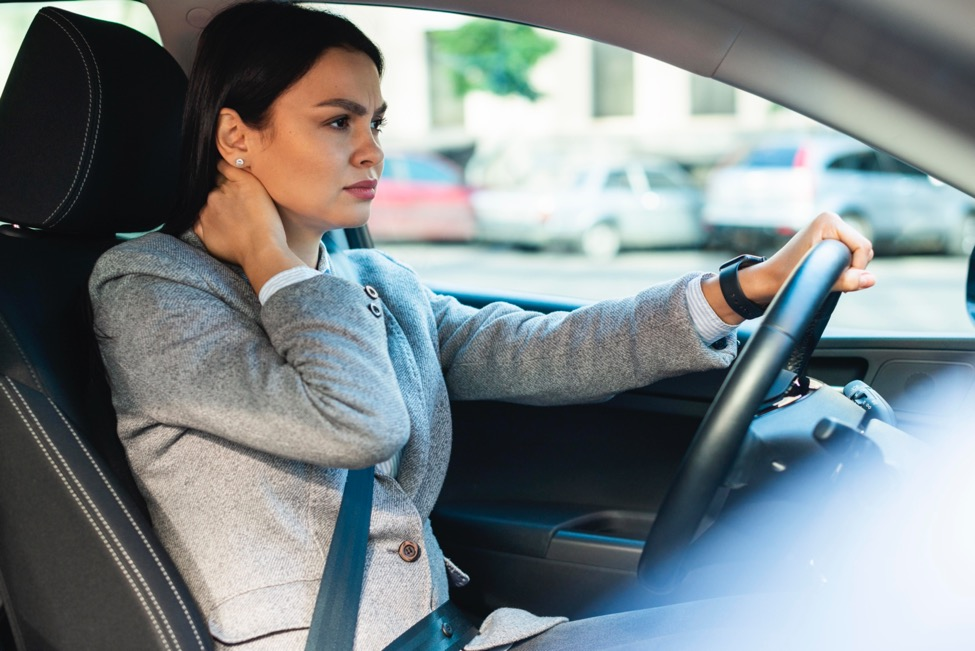 A woman stretches her neck sideways with her hand on the opposite side.