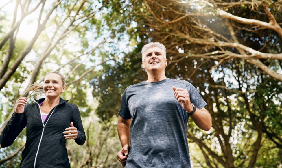 a couple dressed in fitness attire running with trees in the background