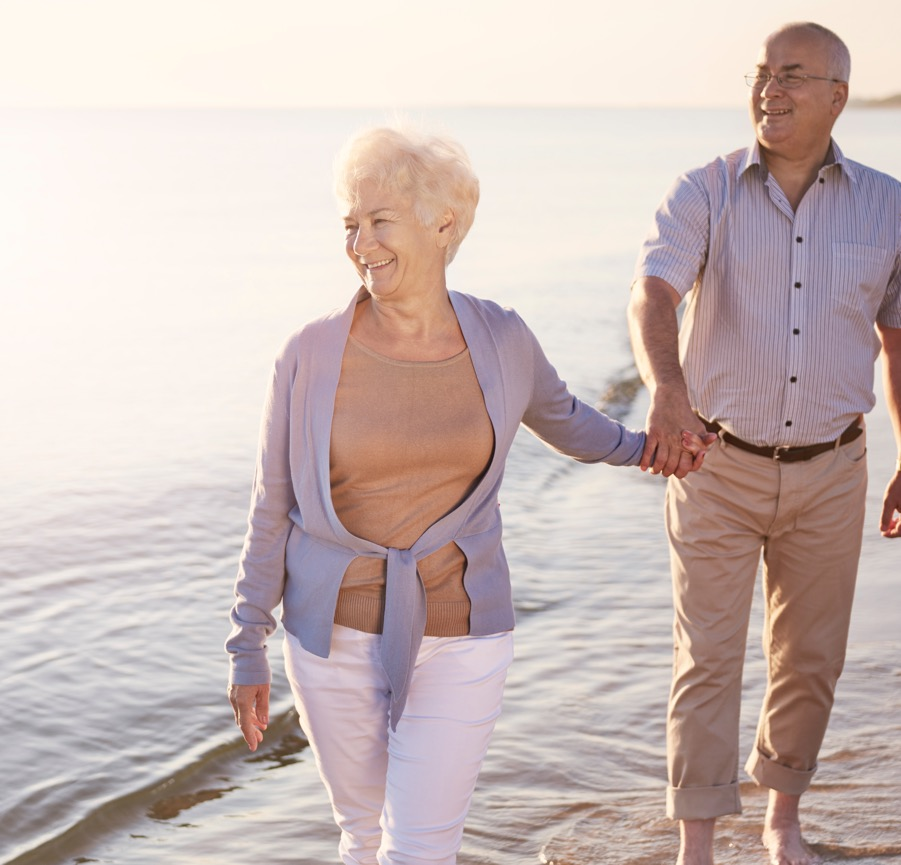 An elderly woman and man walk in the water along a beach