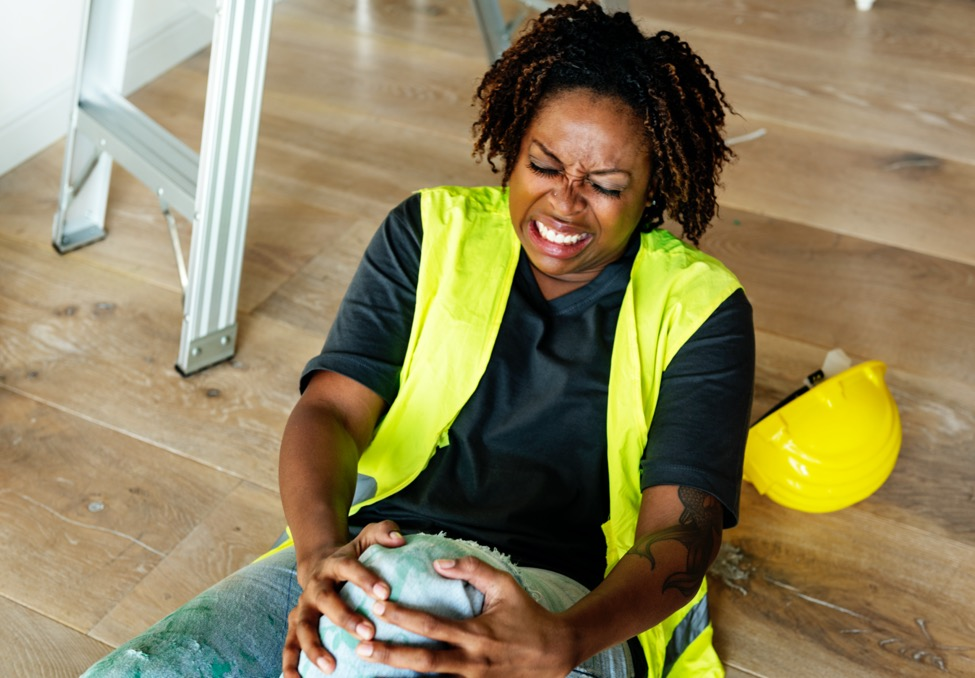 A woman sits on the floor grabbing her knee in pain