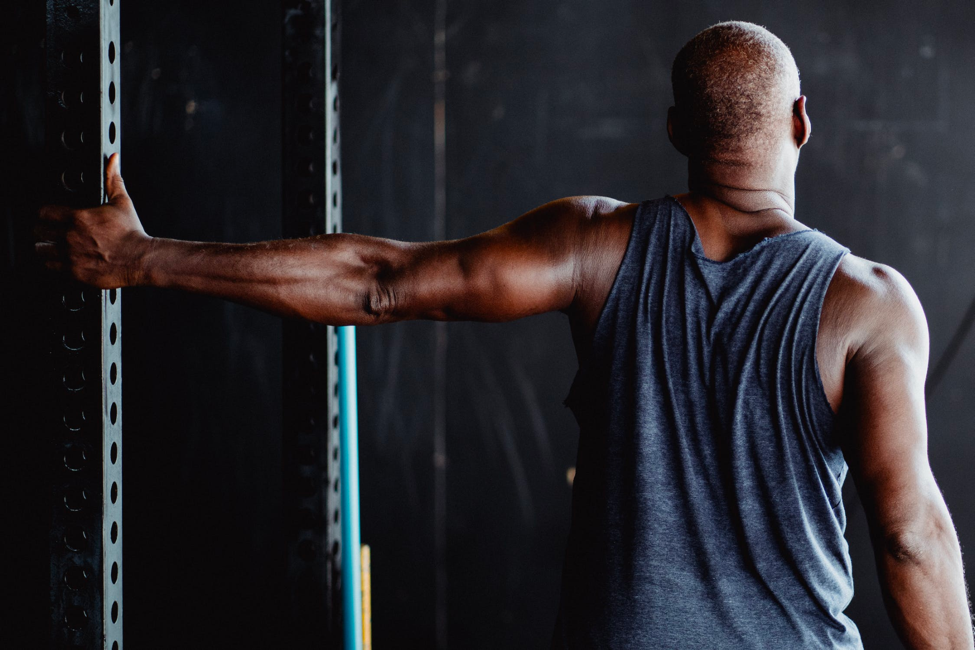 A healthy older man stretches out his shoulder at the gym. 