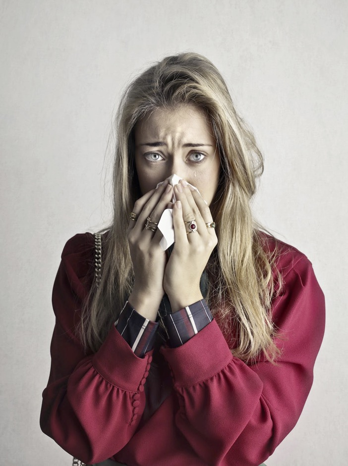 A woman blows her nose into a paper tissue.