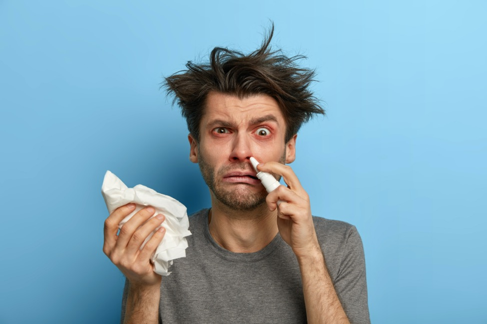 A man holding tissues in one hand and nose spray in the other. 