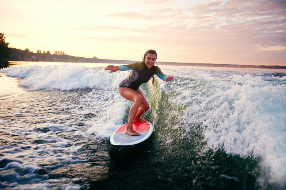 A woman surfing with sunset behind her.