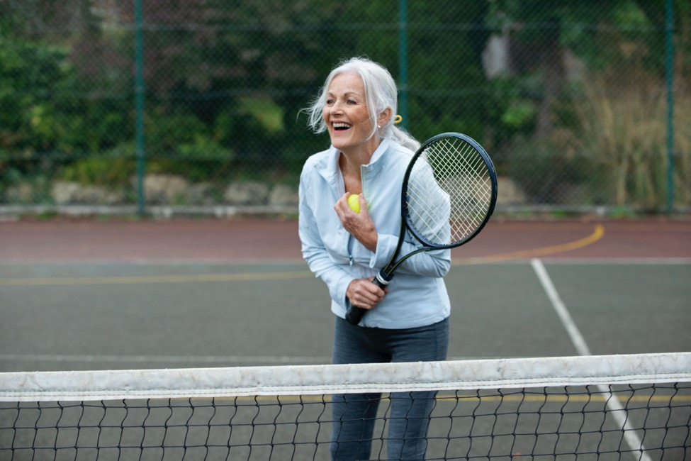 woman stands laughing on a tennis court