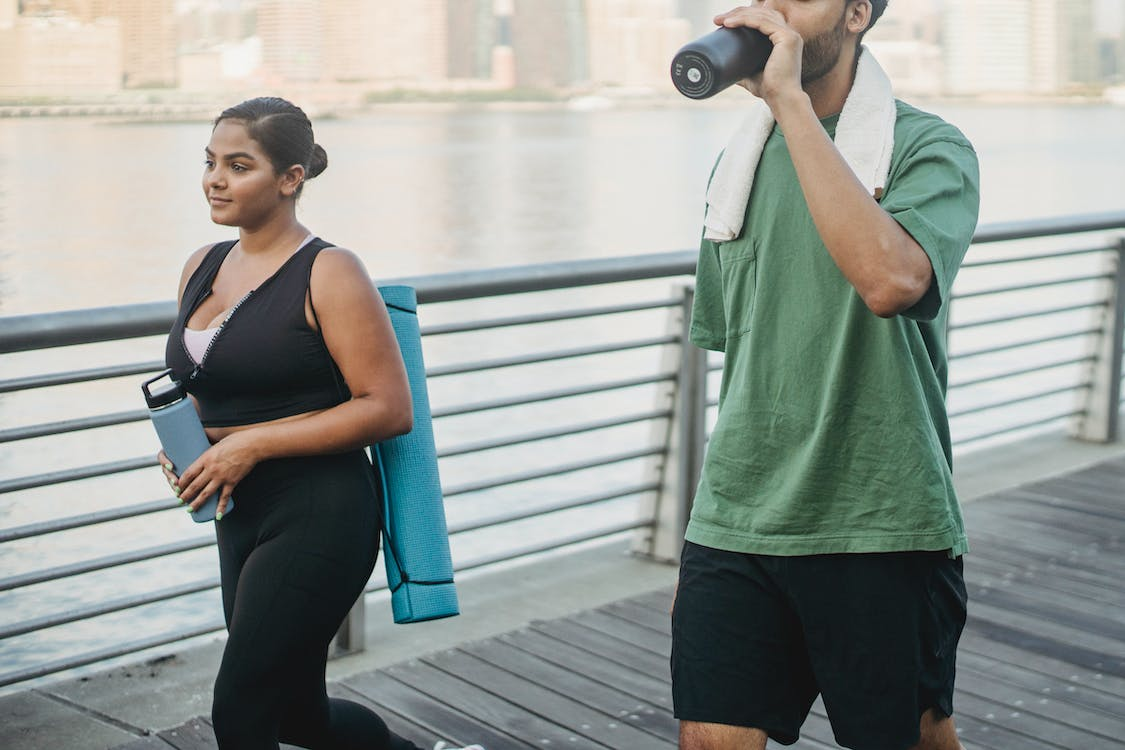 a woman and man walking while he drinks water after his workout