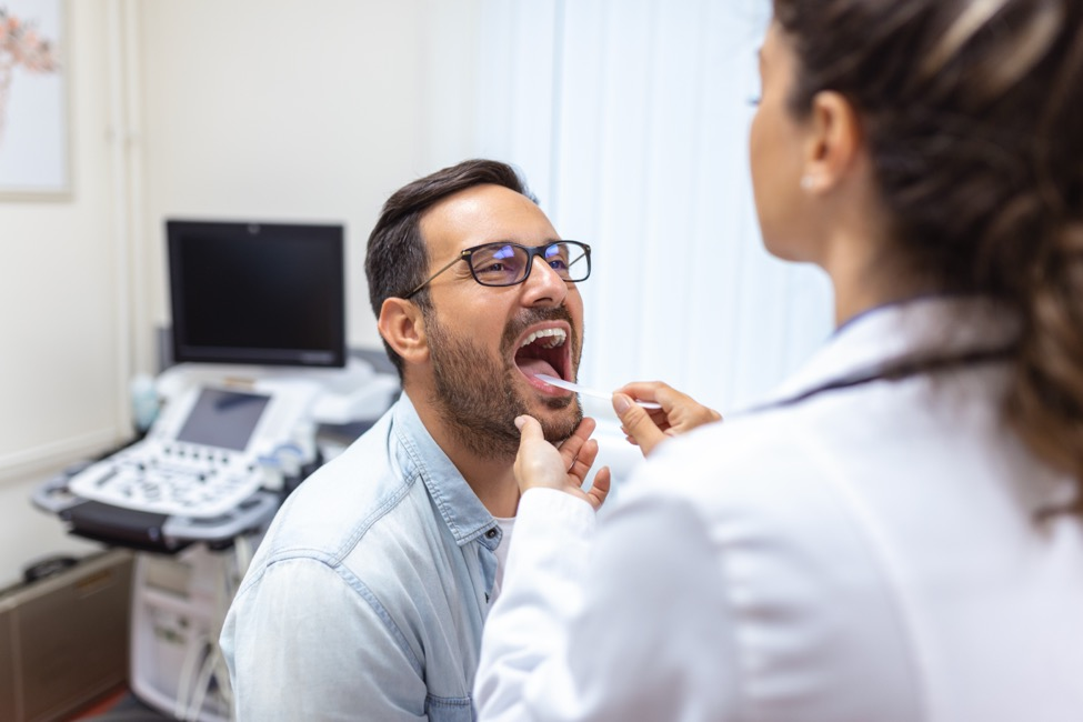 an ENT specialist examines a man’s throat using a tongue depressor