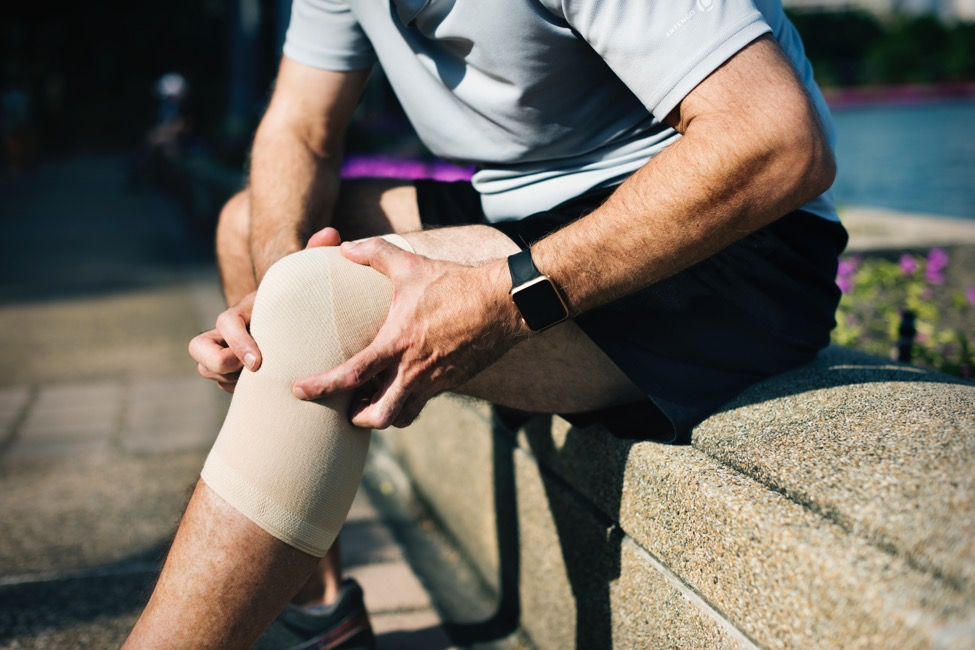 a man sittin on wall grabbing his bandaged knee after surgery