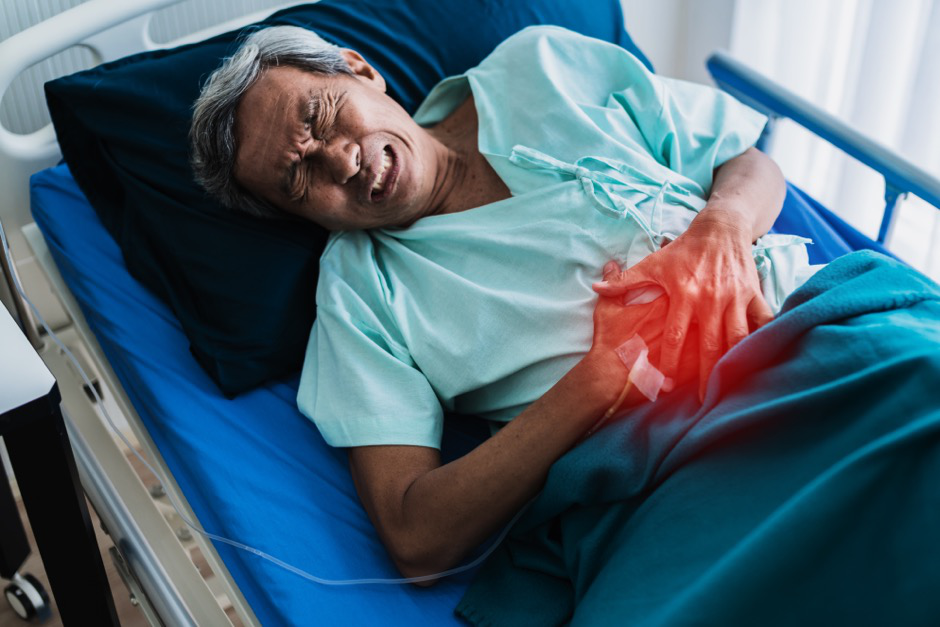 Man in a hospital bed, holding his abdomen in pain.