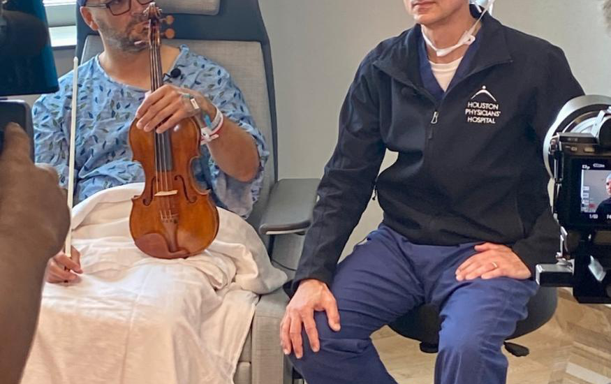 Essential tremor patient holding violin while seated with Dr. Greg Bonnen.