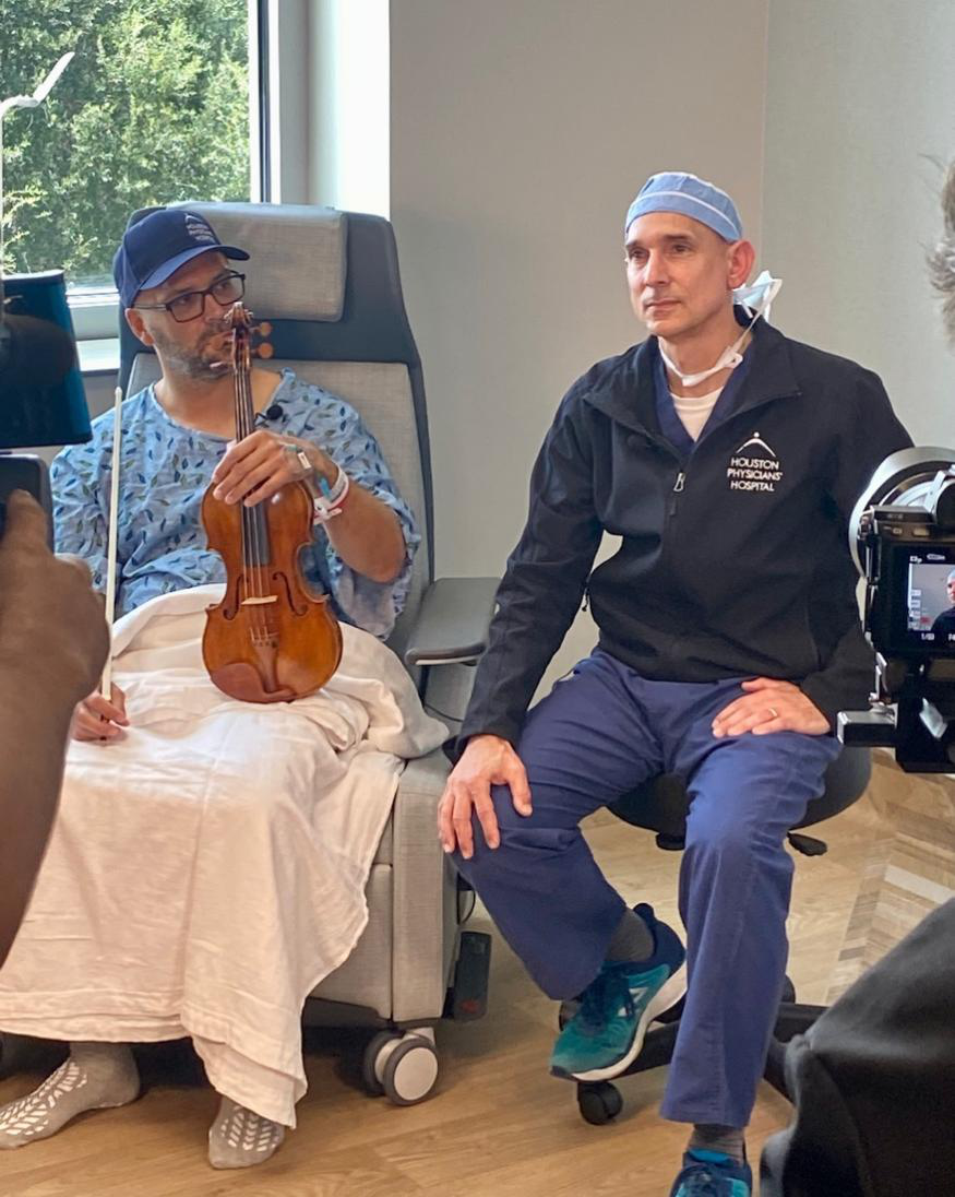 Essential tremor patient holding violin while seated with Dr. Greg Bonnen.
