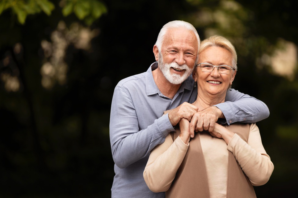 A senior couple stand with his arms around her neck, demonstrating the benefits of minimally invasive orthopedic surgery.
