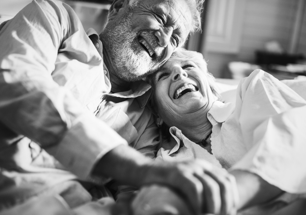 A patient smiling and laying down with her partner while recovering from minimally invasive orthopedic surgery.