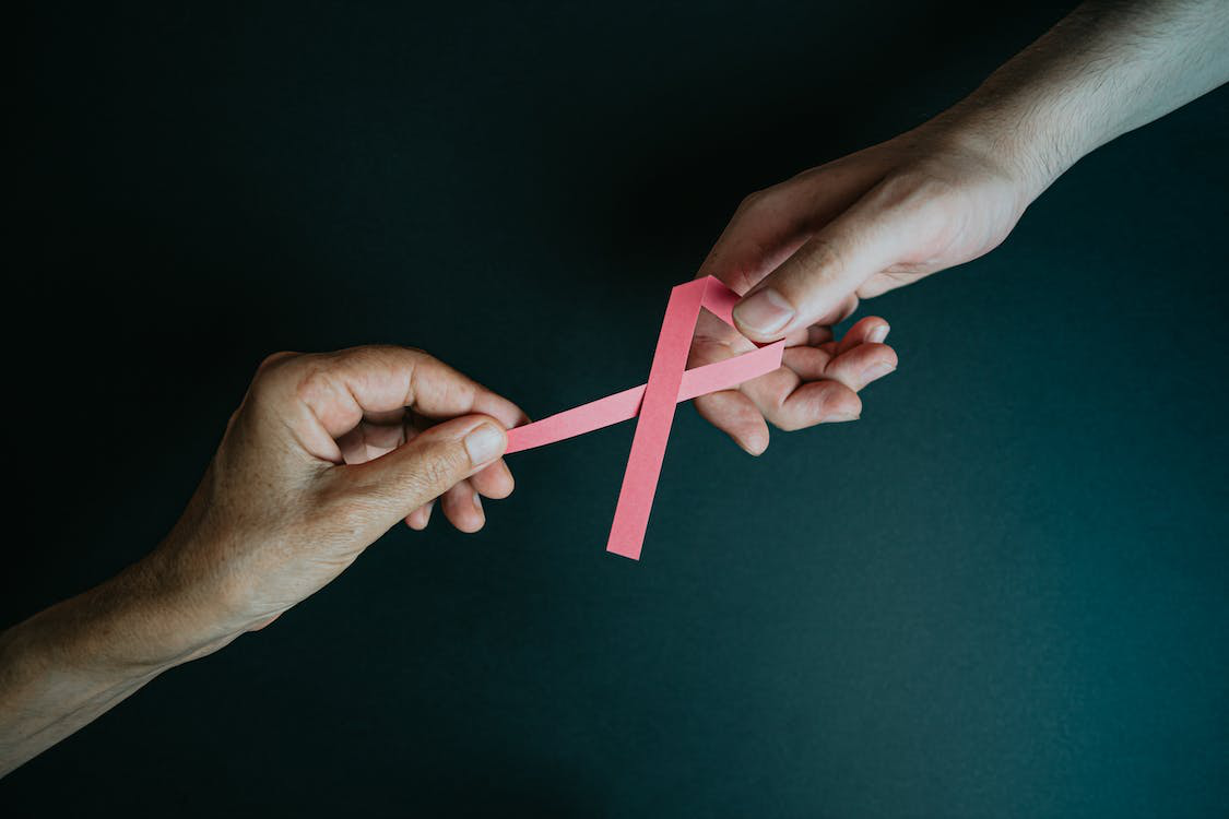 Hands holding a pink paper ribbon signifying breast cancer.