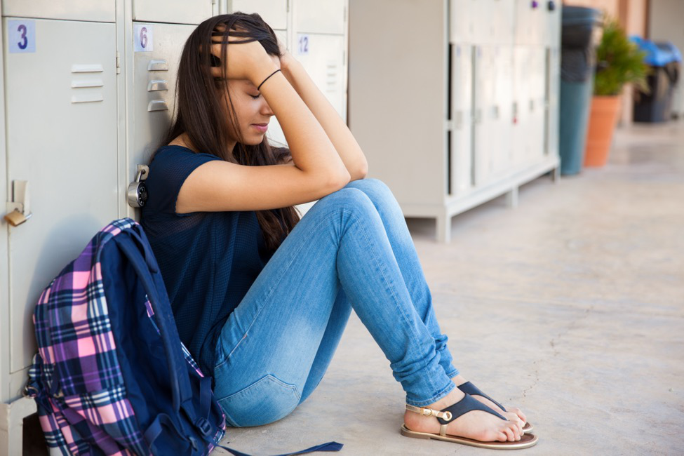 A teenager experiencing chronic pain sits in front of her locker at school