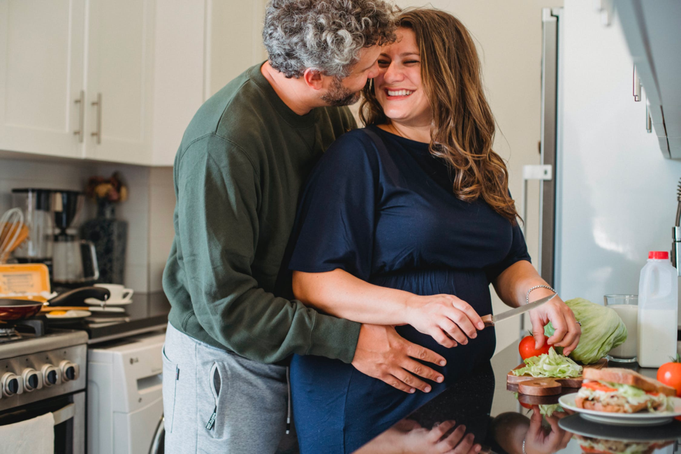 A healthy, happy-looking adult couple smiles while working in the kitchen.