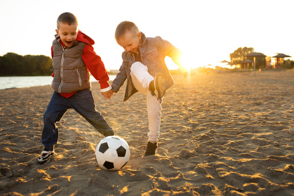 two boys play soccer on the beach.