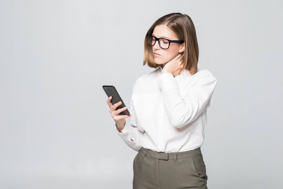 A woman holds her neck while looking at her mobile device.