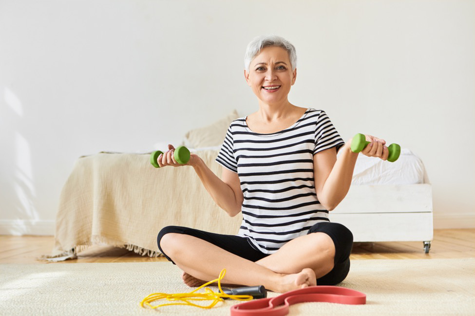 a woman in a striped shirt sits with legs crossed holding light dumbbell weights.