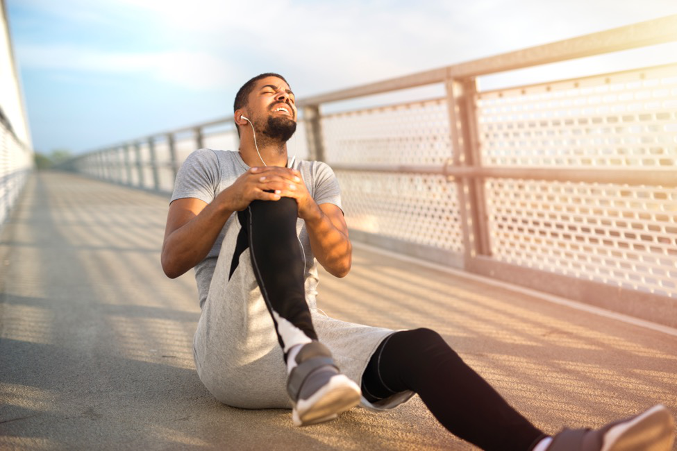 a runner on a bridge sits on the ground grabbing his knee in pain. 