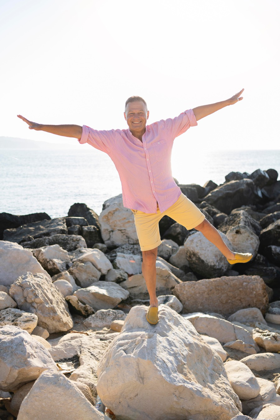 A man in a pink shirt balancing on one leg while standing on a rock