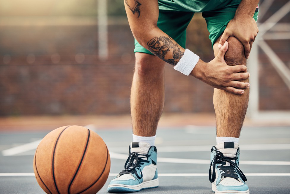 An amateur basketball player grabs his knee on the basketball court.
