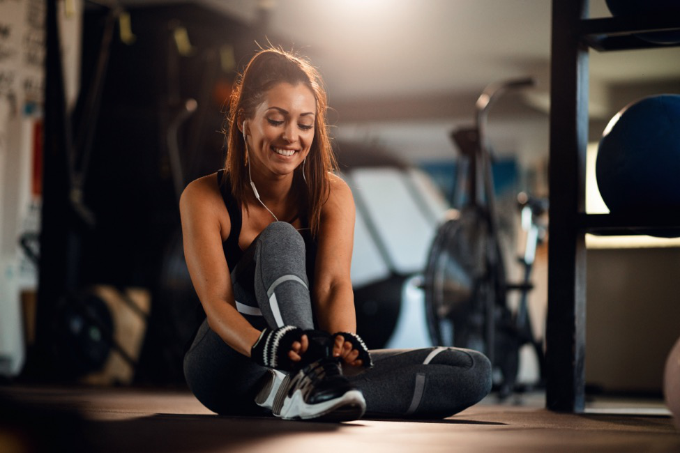 A woman tying her shoe on the floor of a gym.