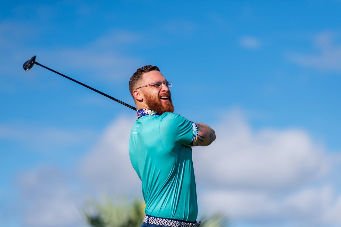 A man with a beard finishes his golf swing