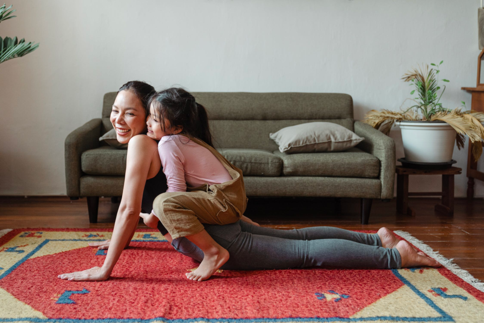 A young mother works out with her daughter while performing a stretch on the floor.