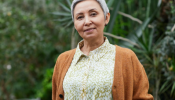 A healthy older woman wearing a dress and a cardigan smiles for the camera.