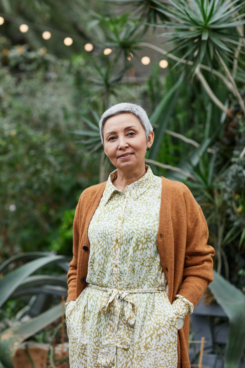 A healthy older woman wearing a dress and a cardigan smiles for the camera.