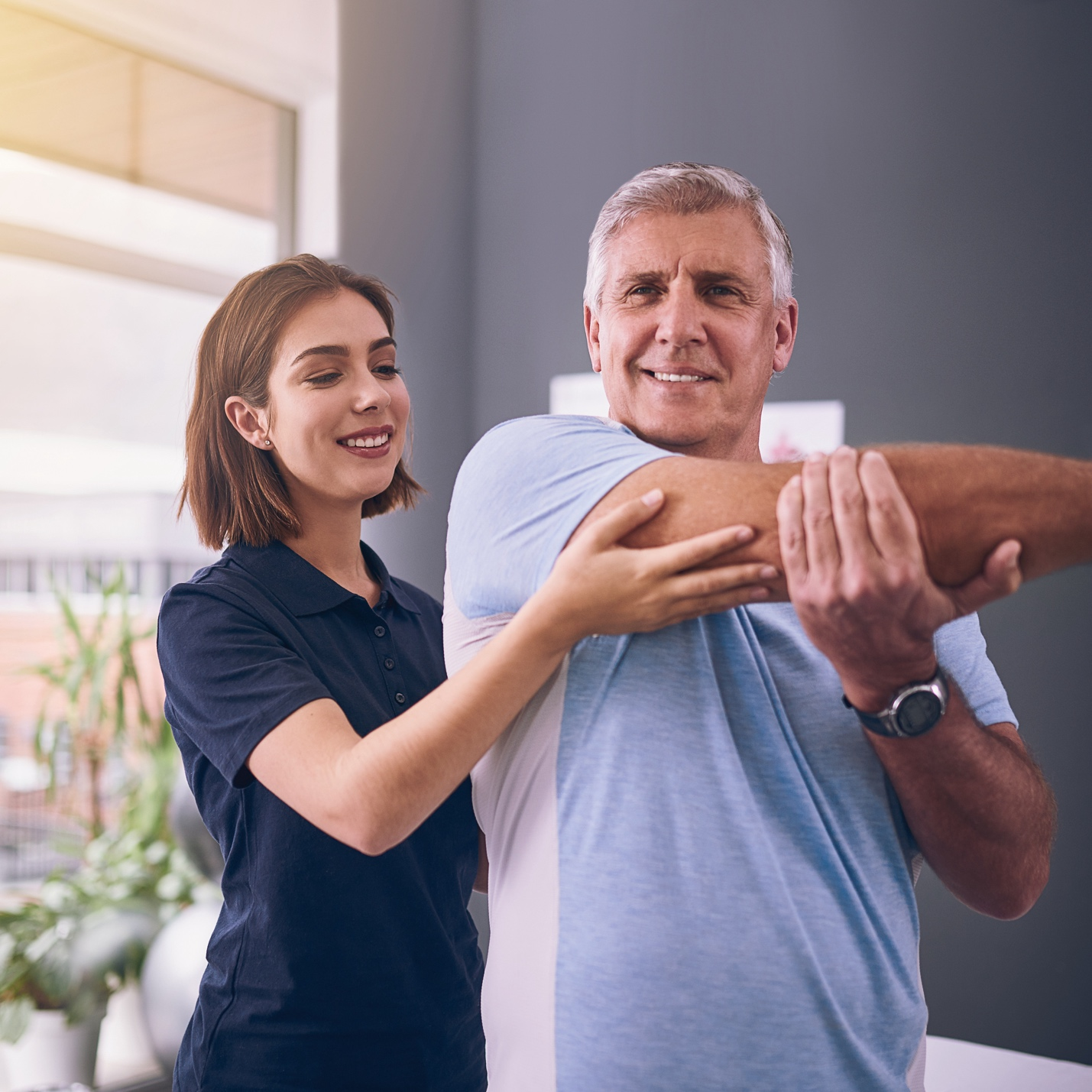 A woman physical therapist supervising a man doing a shoulder stretch