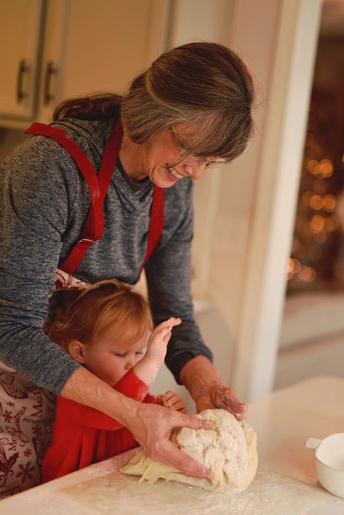 a happy older woman kneading dough with a young child in the kitchen