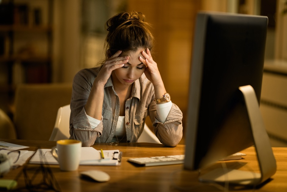 a woman with her fingertips pressed against her forehead looks stressed sitting at her desk