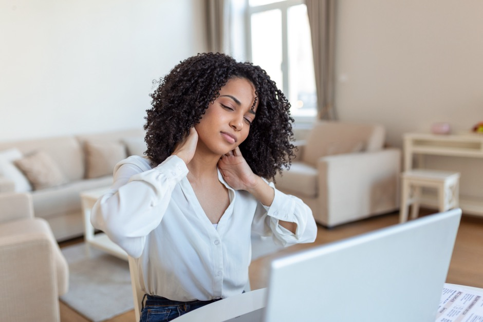 a woman sitting at her desk holds her neck in pain