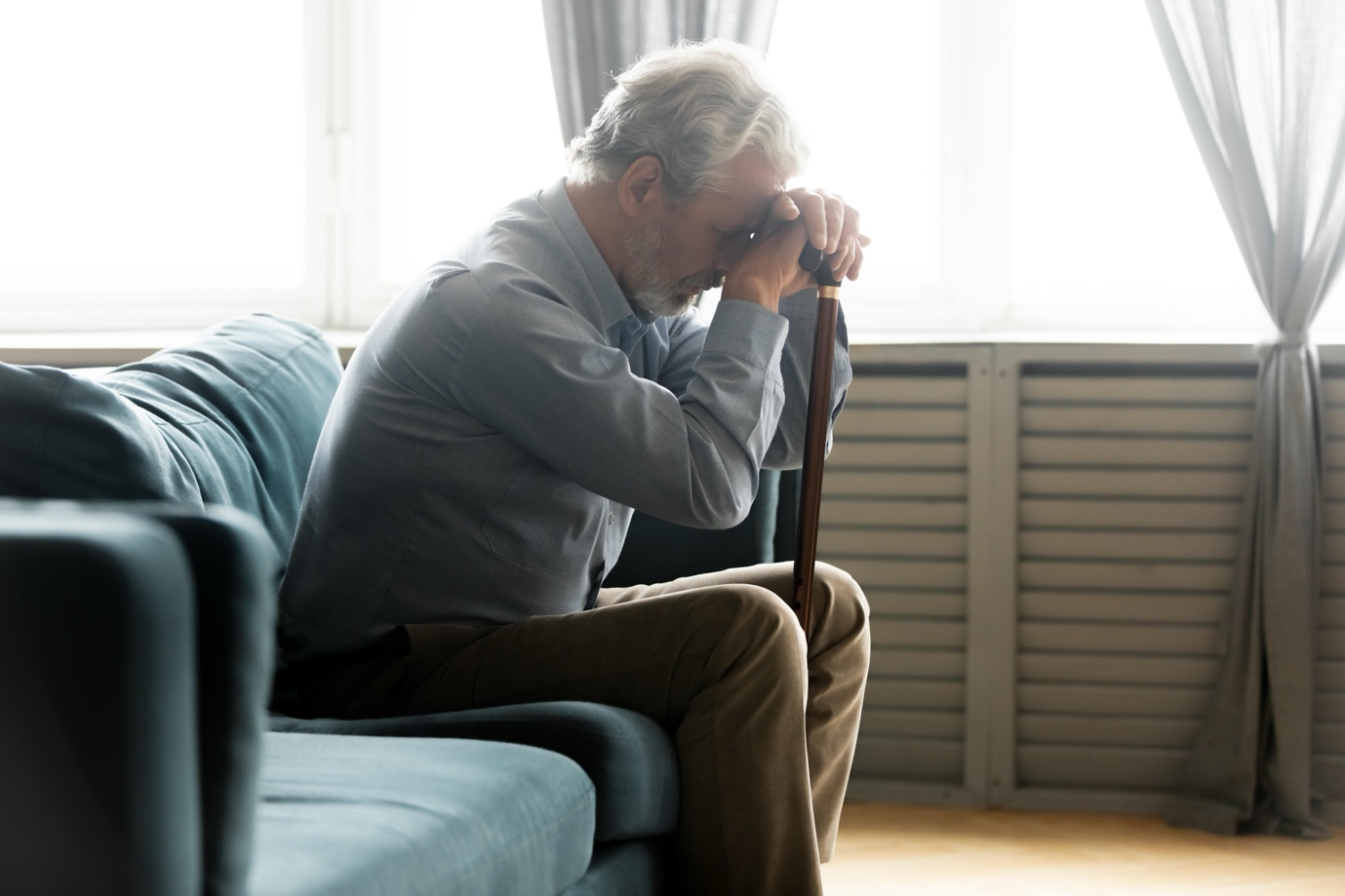 a man sits on a couch with his head resting on his cane