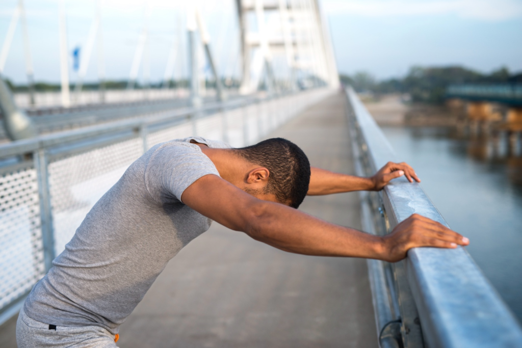 a young man experiencing dizziness holding on to a rail on a bridge