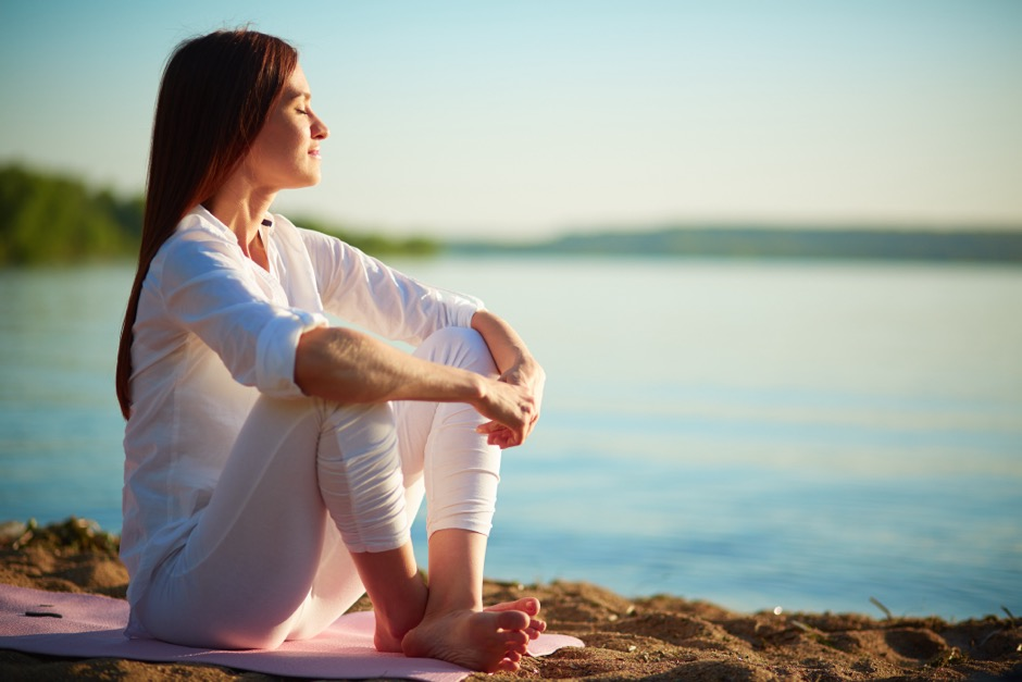 A woman relaxes on a yoga mat while sitting by the water.