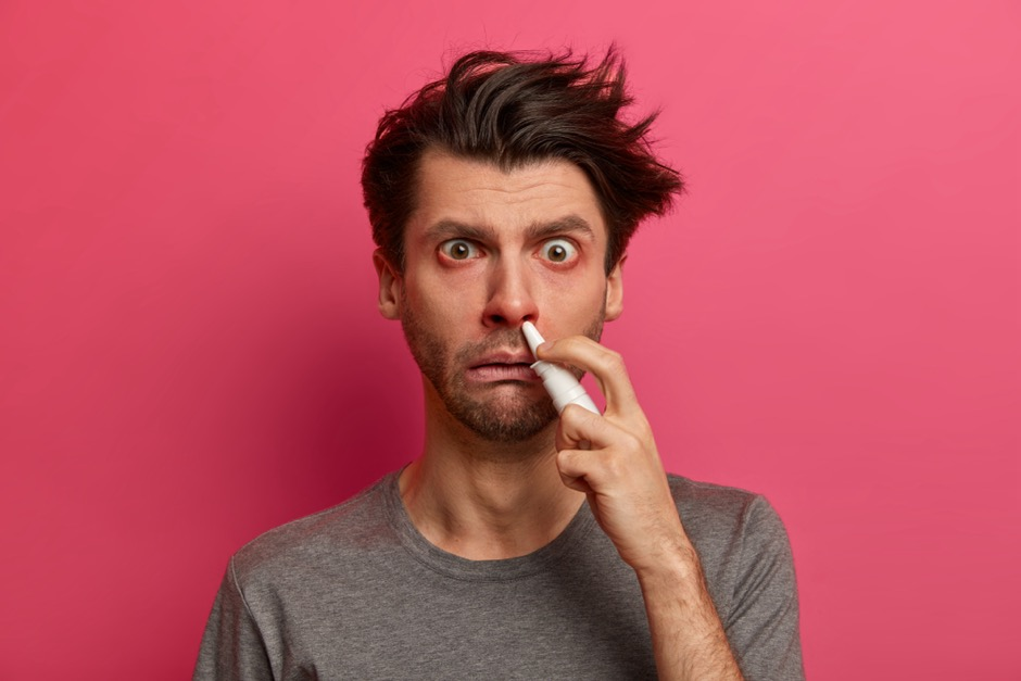A man suffering from allergies holds nasal spray to his nose.