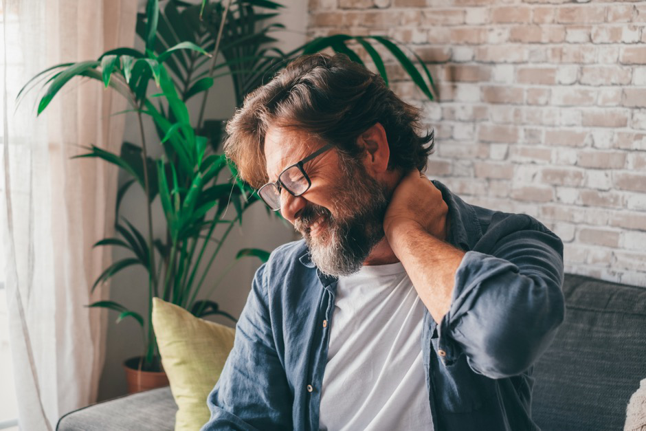 A man holding his neck in pain while sitting on a couch