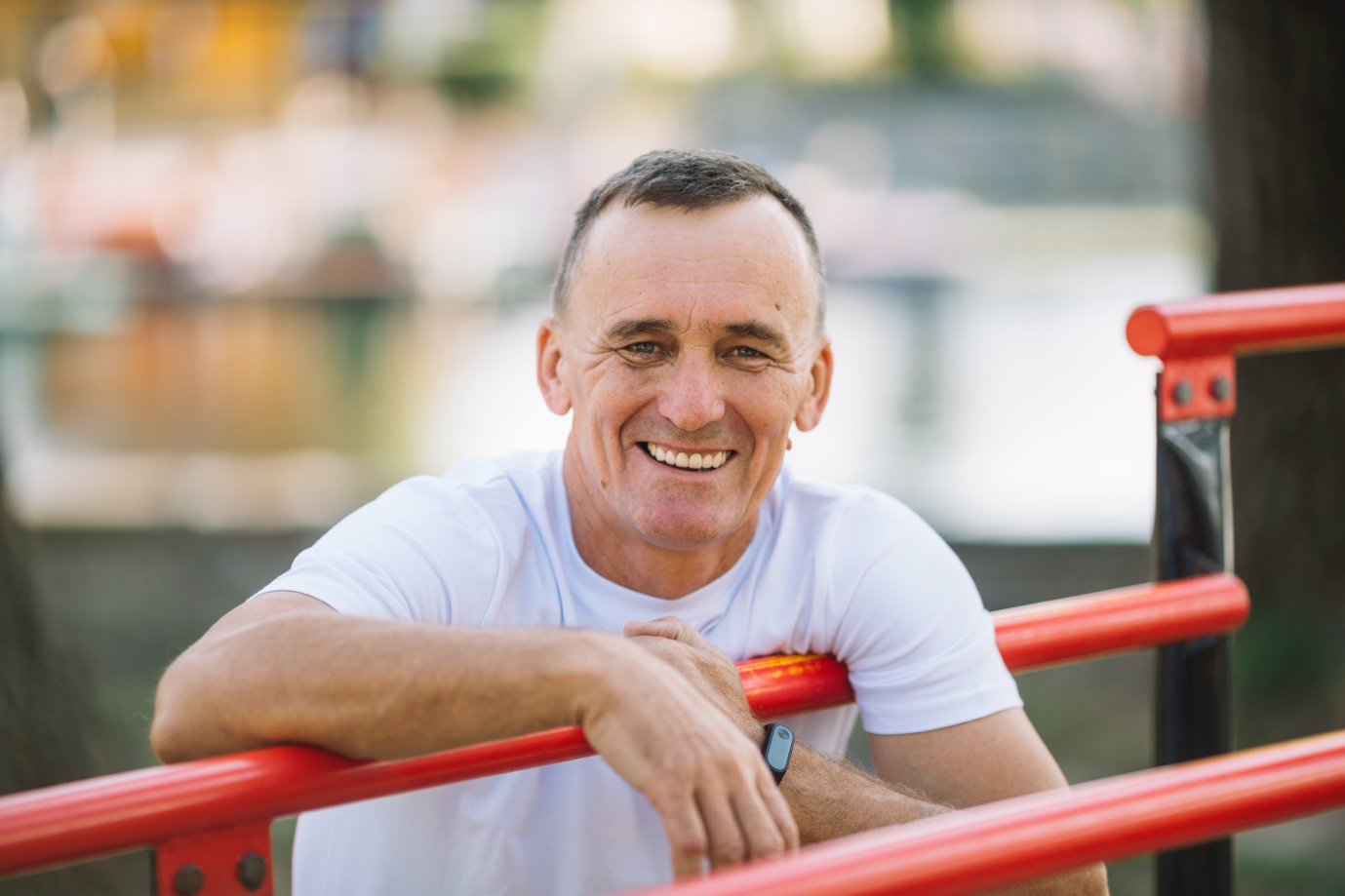 A man smiling and casually leaning on red playground equipment