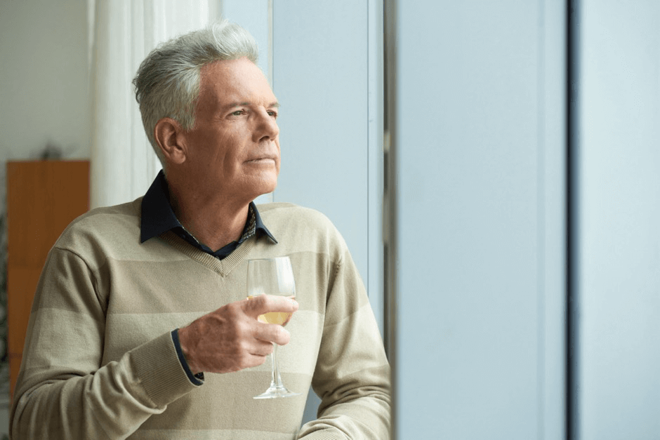 An older man leaning against a railing with a glass of wine.